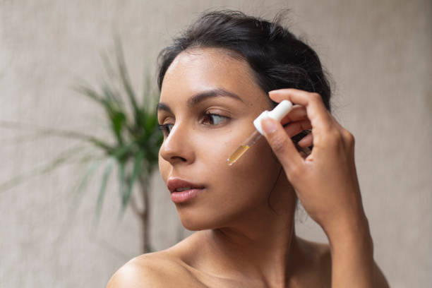 Woman applying facial serum in front of a plant background.