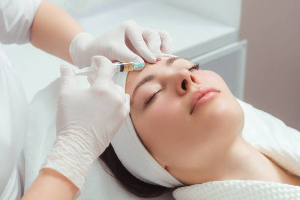 Professional administering facial treatment with syringe to a relaxed female patient in a modern clinic setting