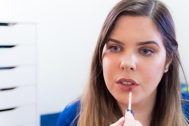 Woman applying lip gloss in office setting